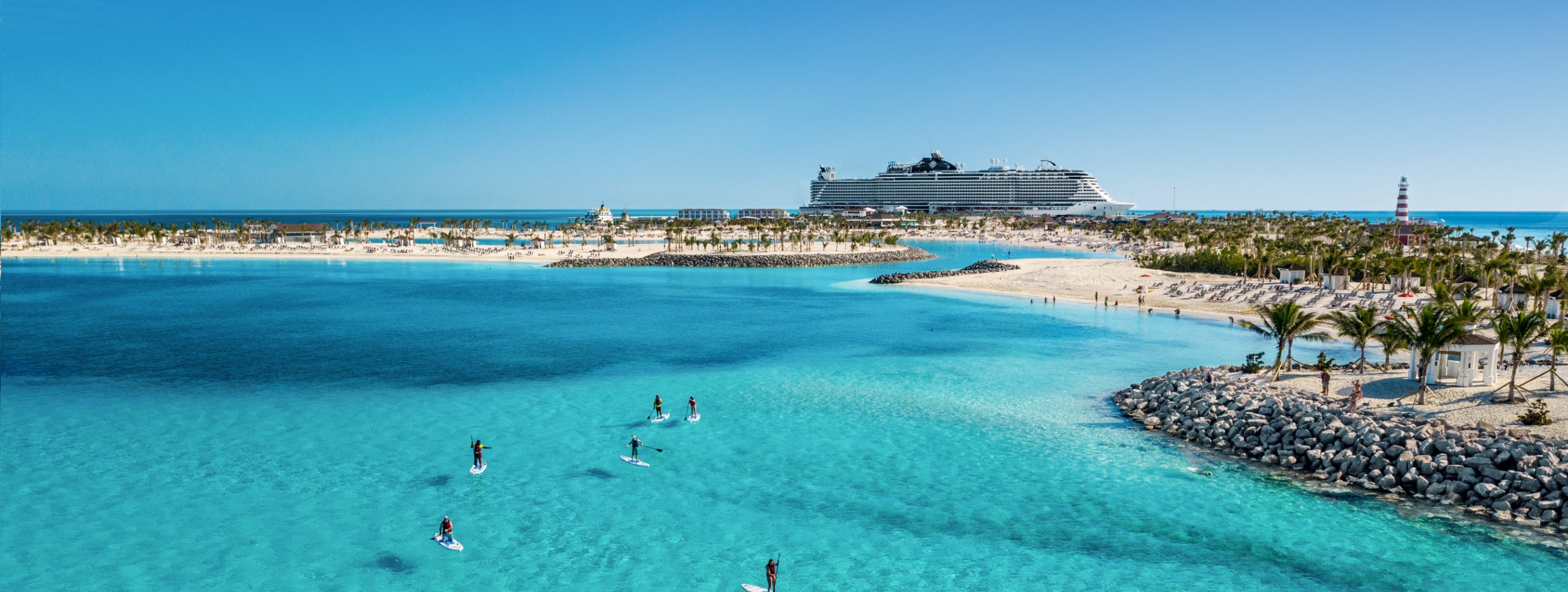 A panoramic view of a sprawling beach with guests paddle boarding in the clear blue water, complemented by the presence of a magnificent cruise ship elegantly positioned on the horizon.