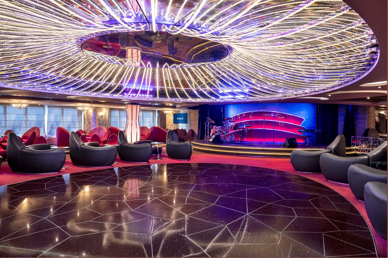 Spacious lounge featuring sofas, a stage and dance floor, inviting relaxation and entertainment | MSC Cruises