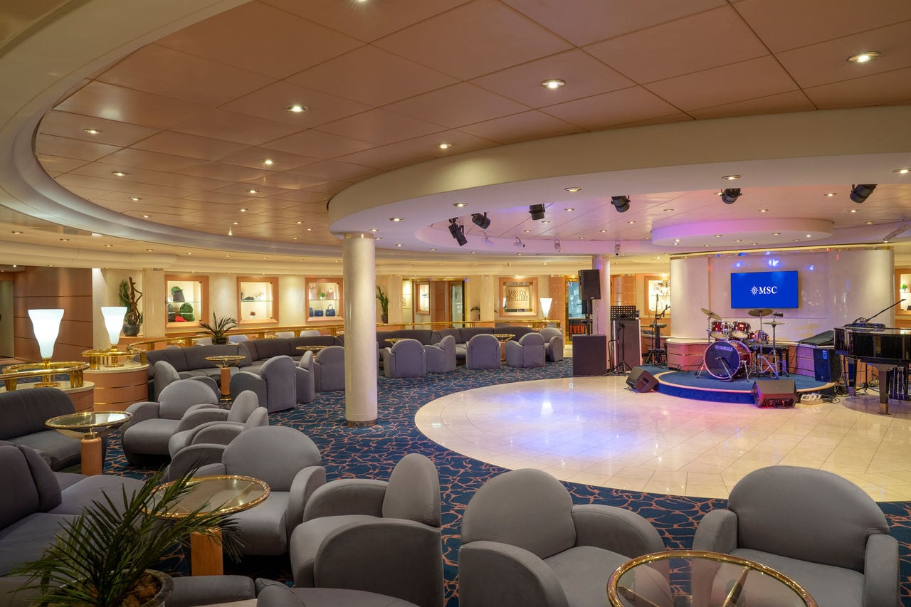 Spacious lounge with armchairs, a stage and piano for relaxing evenings onboard | MSC Cruises