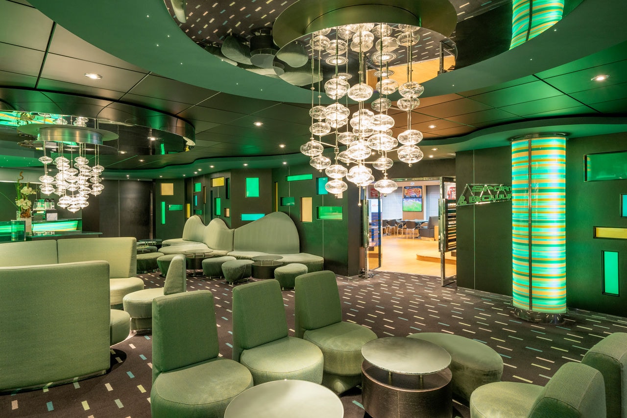 Spacious lounge with green accents, tables, sofas and a bar aboard MSC Preziosa | MSC Cruises