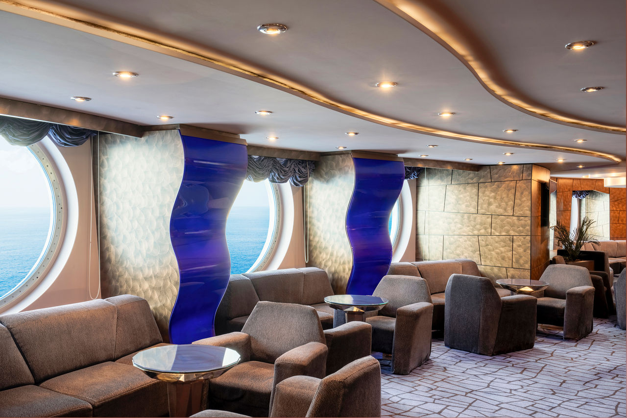 Spacious lounge with large portholes and comfortable seating overlooking the sea | MSC Cruises