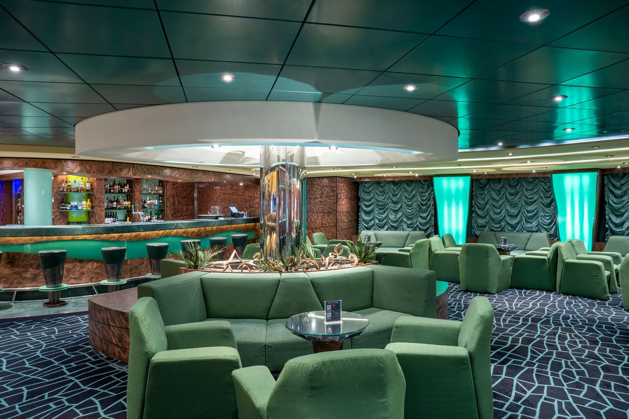 Spacious lounge featuring green armchairs and a central bar area on a cruise ship | MSC Cruises