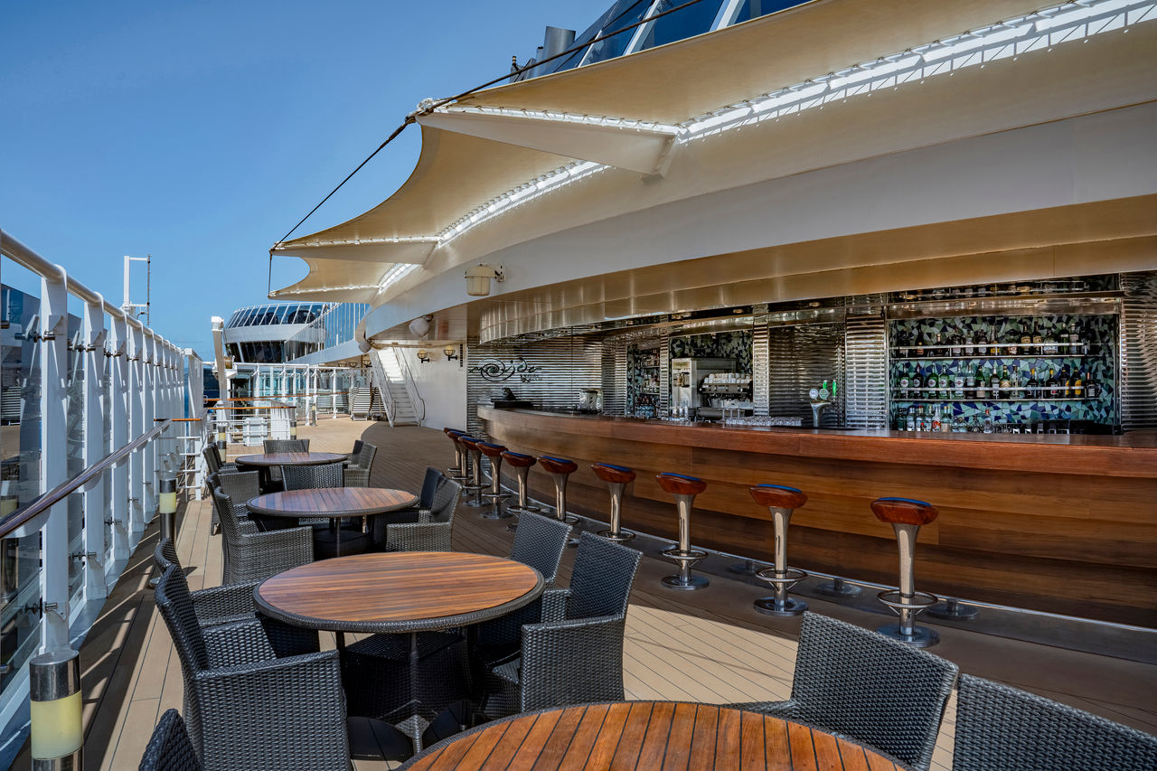 Outdoor seating and bar area on a cruise ship beneath a clear blue sky | MSC Cruises
