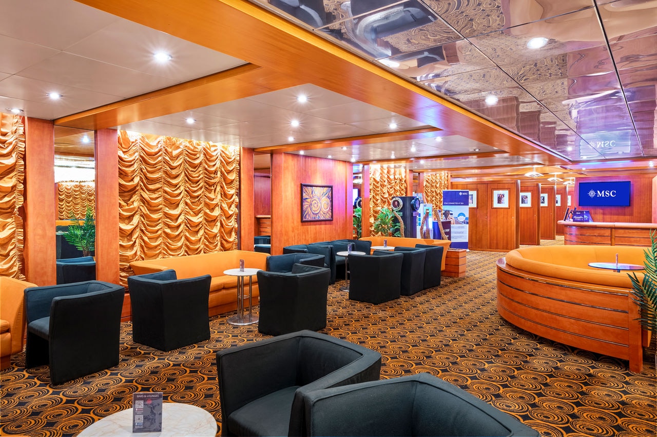 Spacious lounge featuring orange sofas, armchairs and lush plants for relaxing moments | MSC Cruises