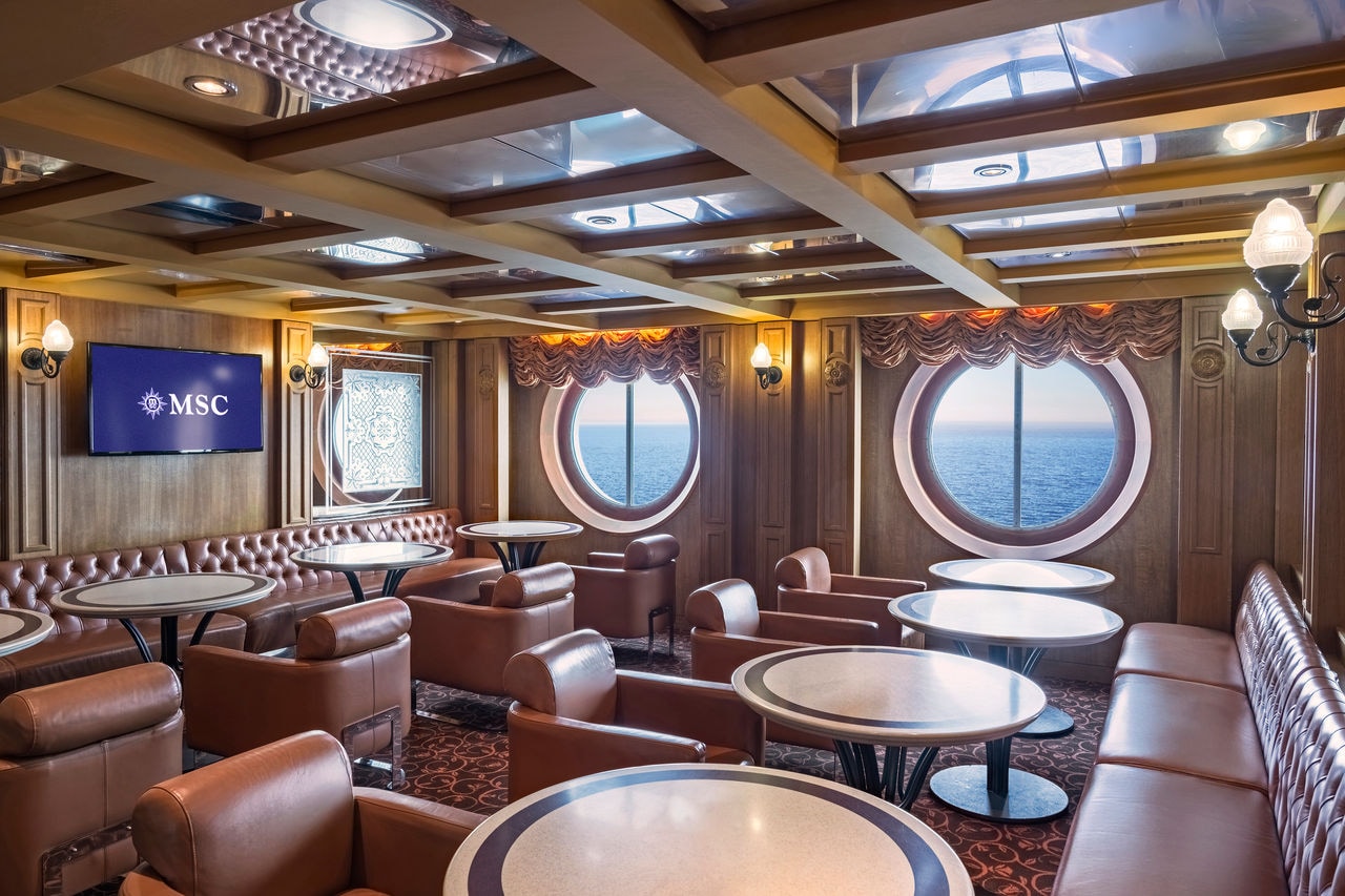 Spacious lounge with round windows, seating and tables overlooking the sea | MSC Cruises