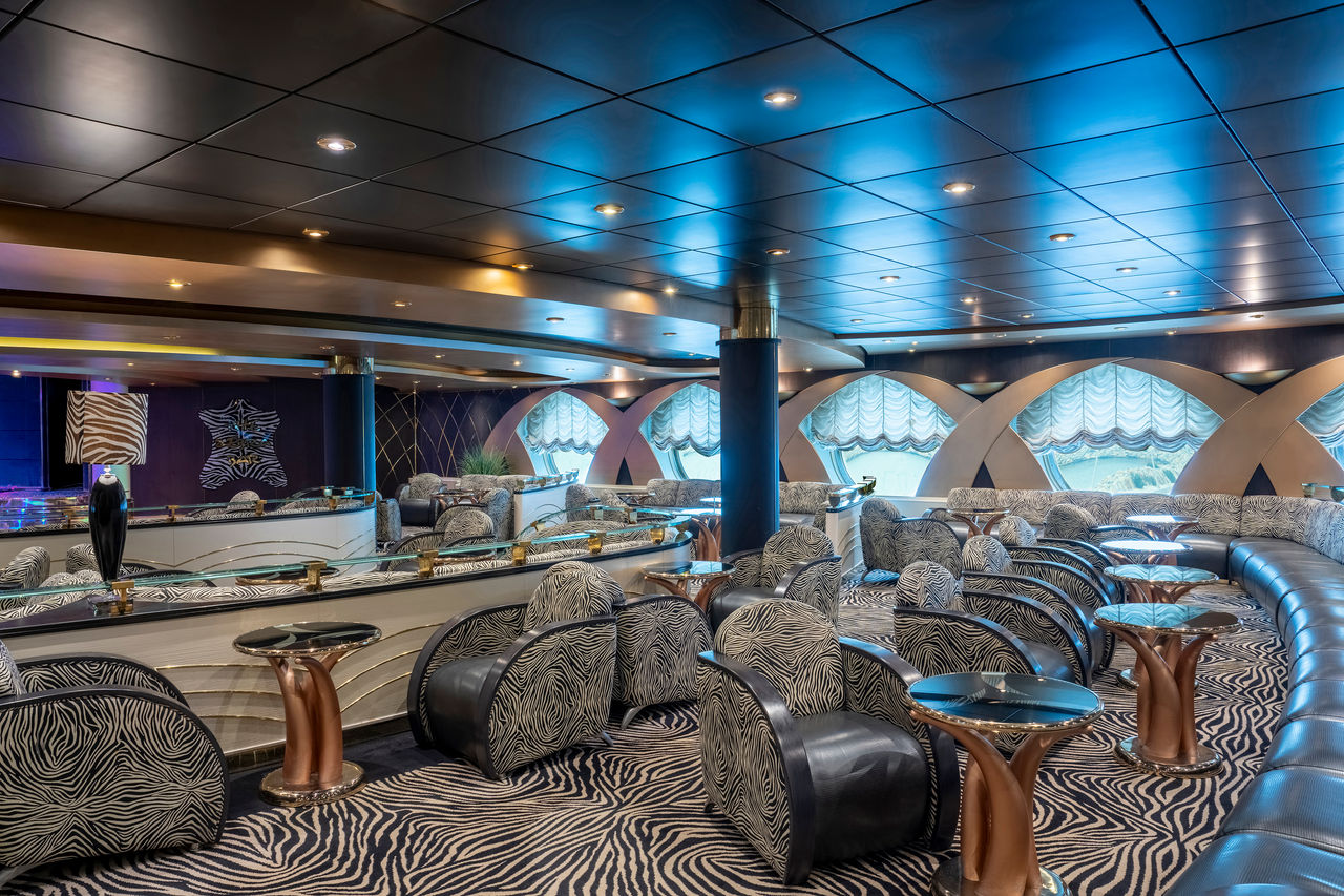 Spacious lounge with sofas, tables and large porthole windows aboard a cruise ship | MSC Cruises