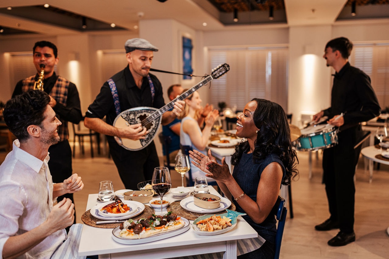 Guests enjoy dinner accompanied by live music in a Greek restaurant setting | MSC Cruises