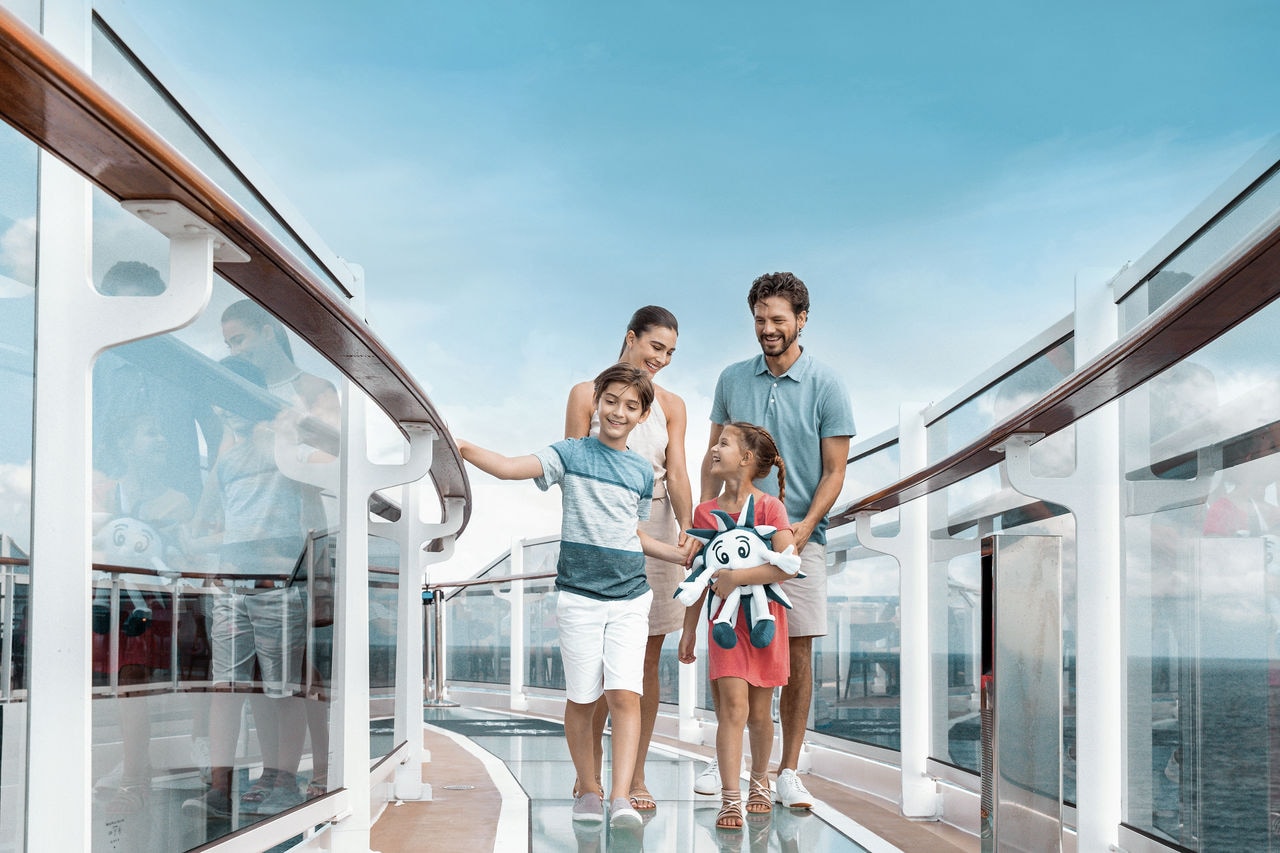 A family walks together on a glass bridge aboard a cruise ship under a clear blue sky | MSC Cruises