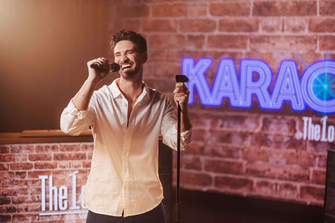 Man singing karaoke in a welcoming lounge with neon sign on MSC World America | MSC Cruises