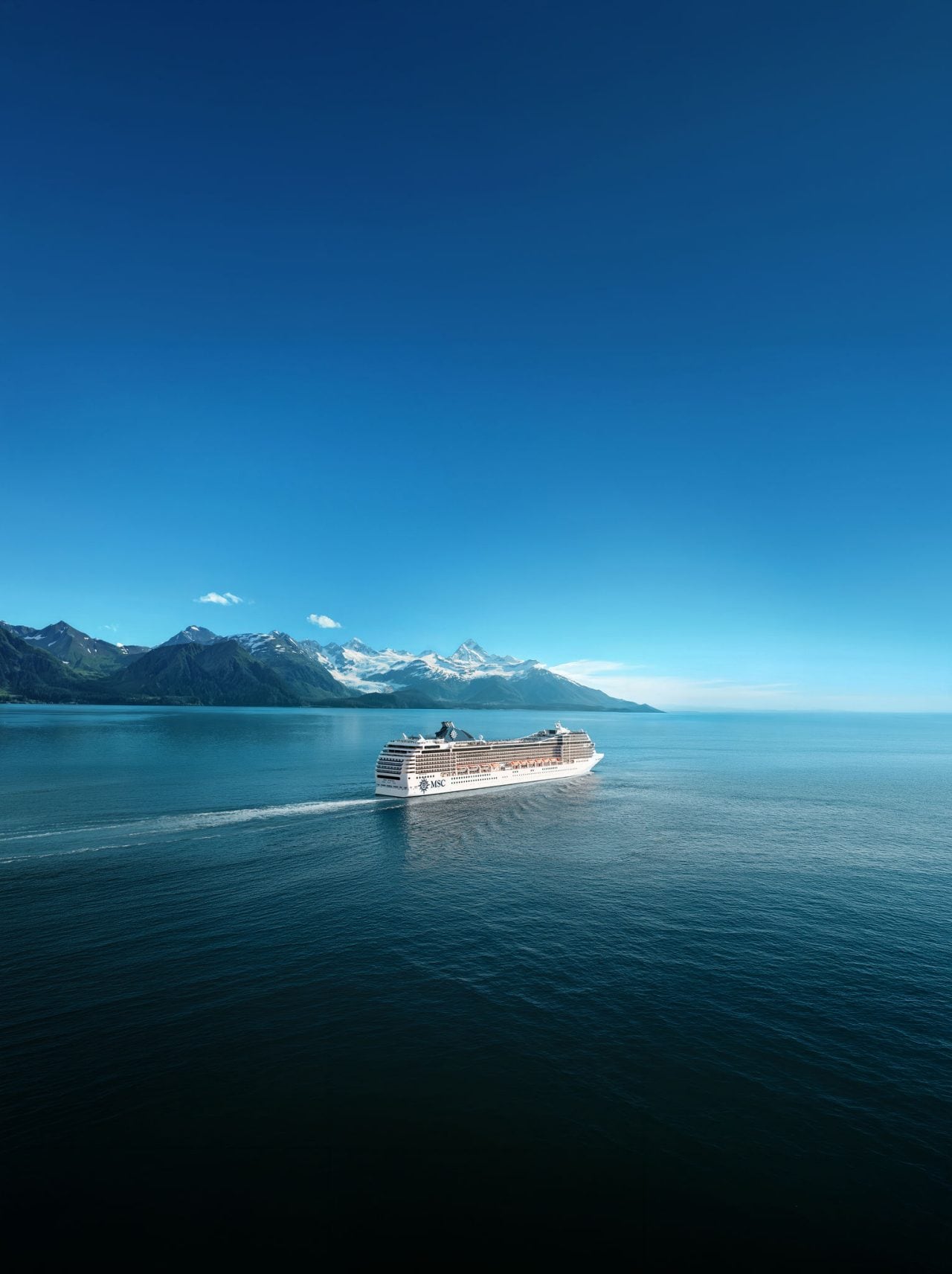 A cruise ship sails across calm waters with snowy mountains and a clear sky in the distance | MSC Cruises