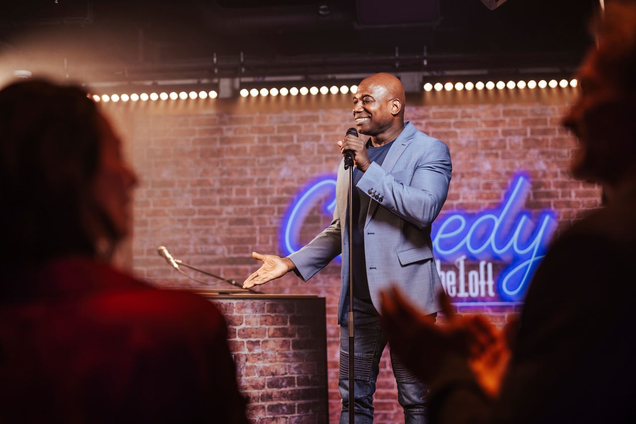 A comedian entertains an applauding audience on stage in a vibrant lounge setting | MSC Cruises