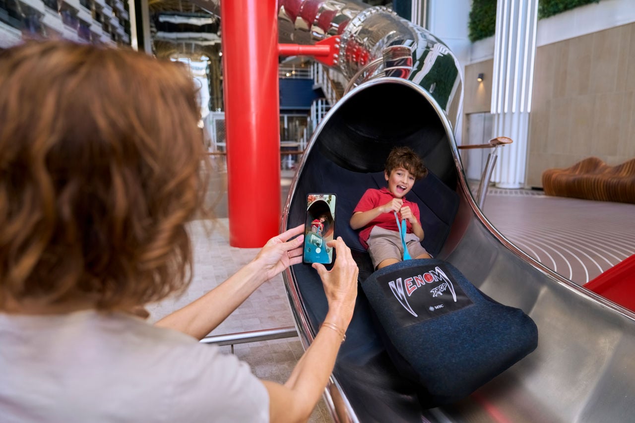 A child enjoys a slide as an adult captures the moment on a smartphone in a lively setting | MSC Cruises